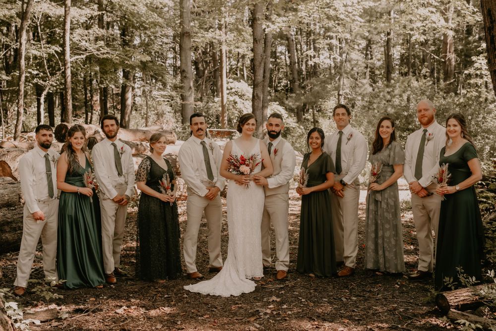 Wedding party poses together in forest wearing coordinated formal attire in muted tones.