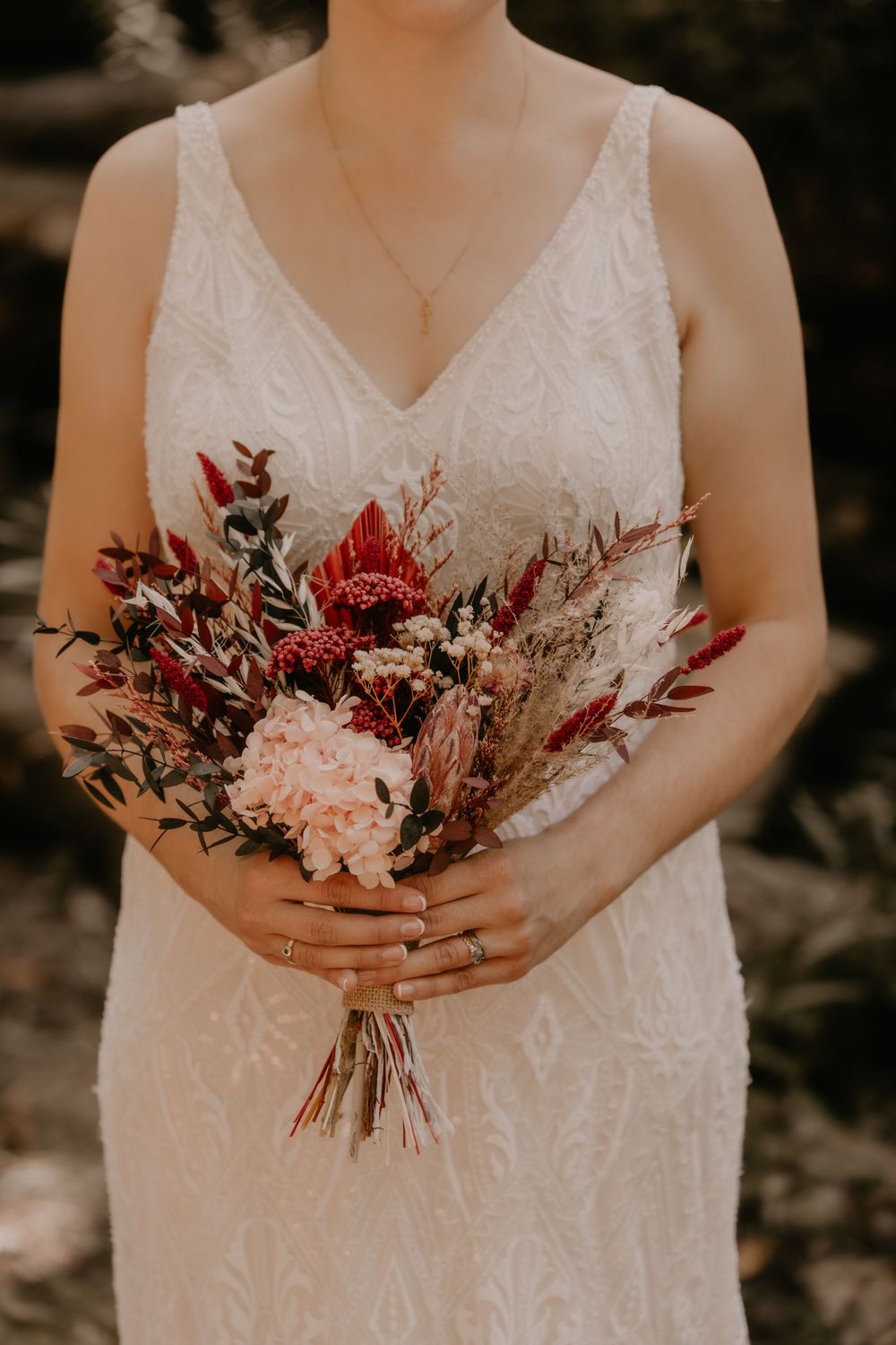 Close-up of bridal bouquet featuring red and pink flowers with mixed greenery.