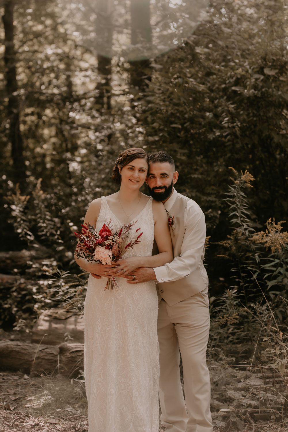 A romantic outdoor wedding portrait of a couple surrounded by forest greenery.