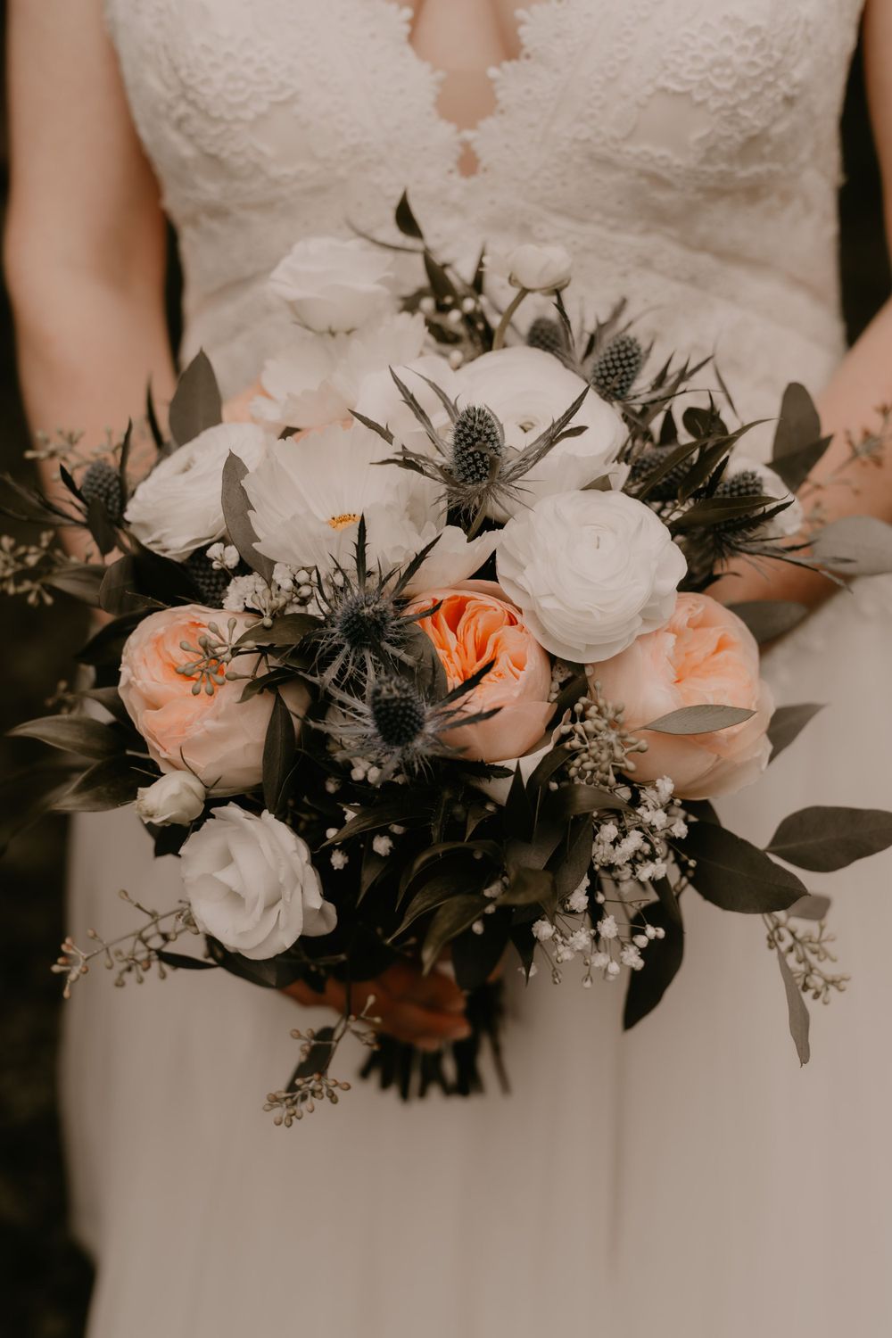 Elegant bridal bouquet with white and peach roses mixed with dark foliage.