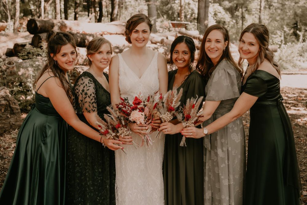 Bride and bridesmaids in forest green dresses show off their bouquets in a group photo.