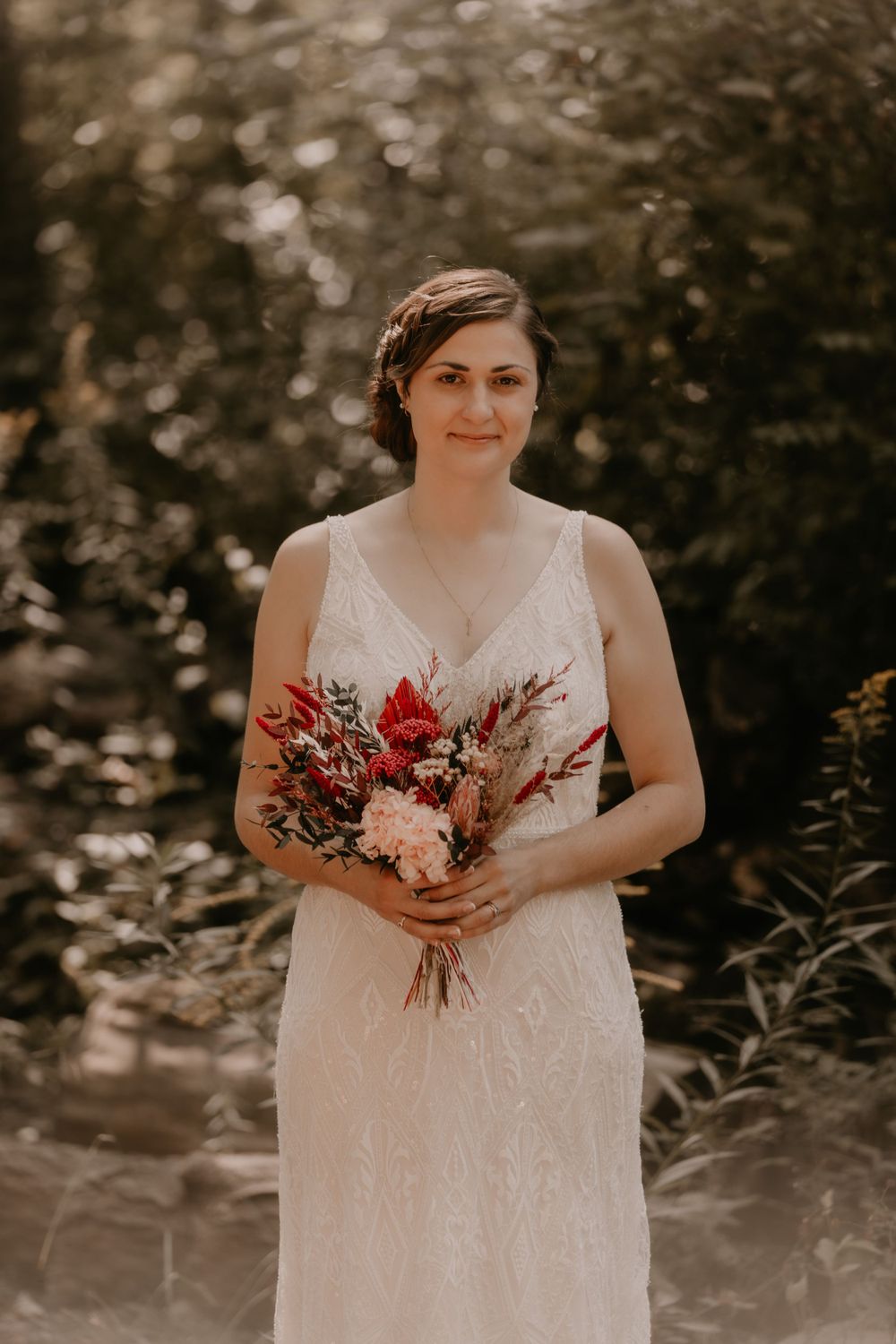Bride in a lace v-neck wedding dress holds a bouquet with red and pink flowers.