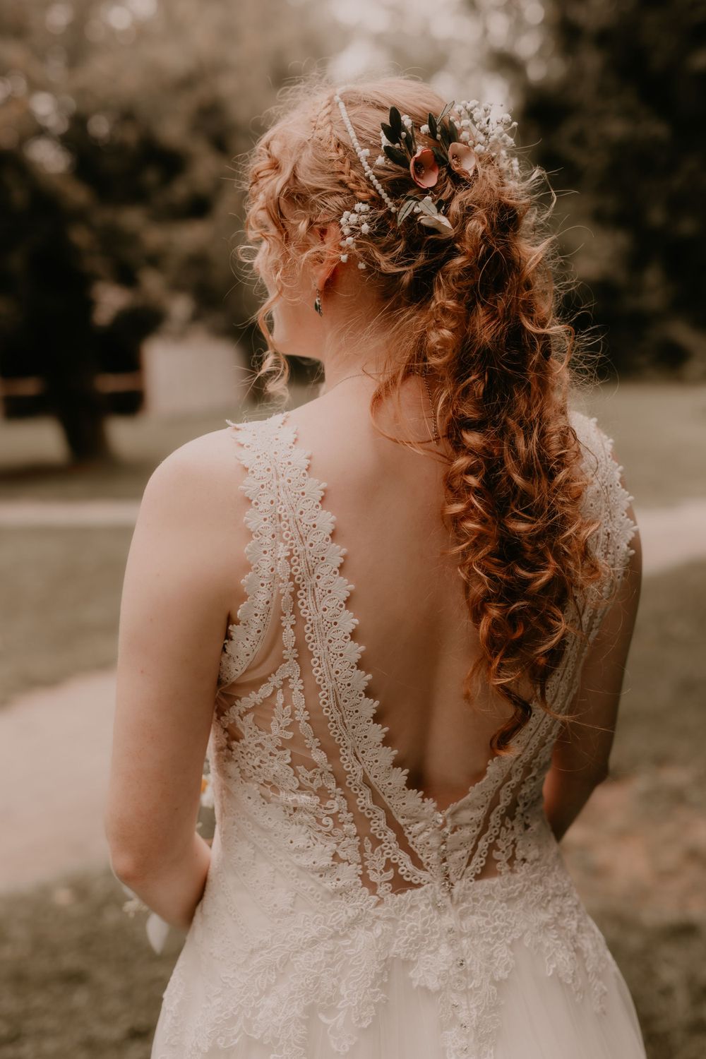 Detailed back view of bride's lace wedding dress and curled hair with floral accessories.