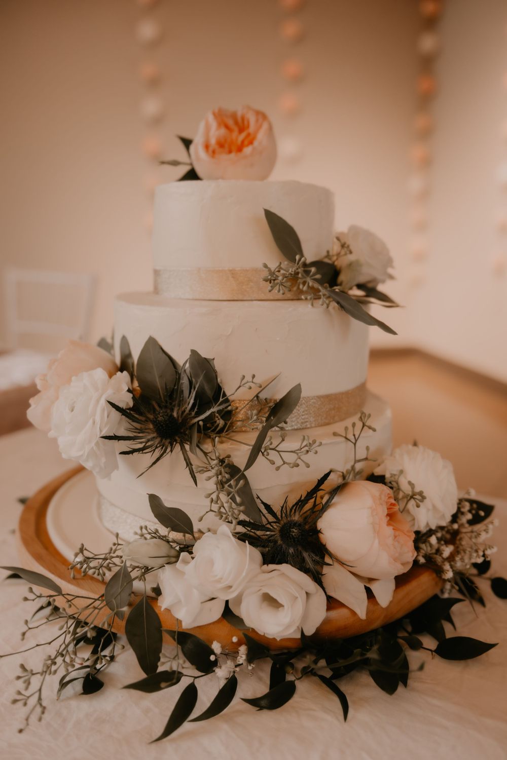 Three-tiered white wedding cake adorned with blush roses, eucalyptus leaves and delicate floral decorations.