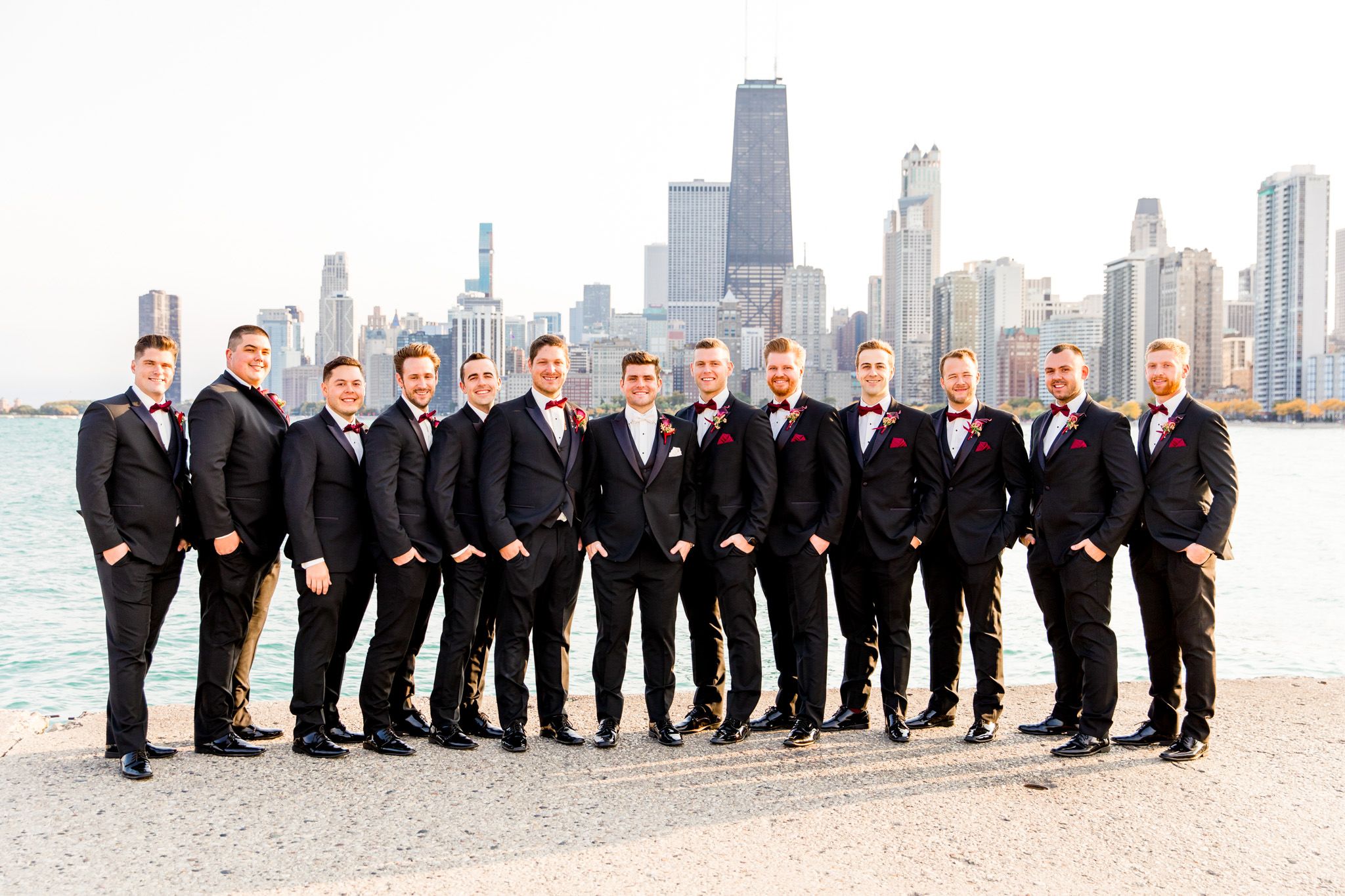 groomsmen with red boutonnieres and black tux pose in front of chicago skyline