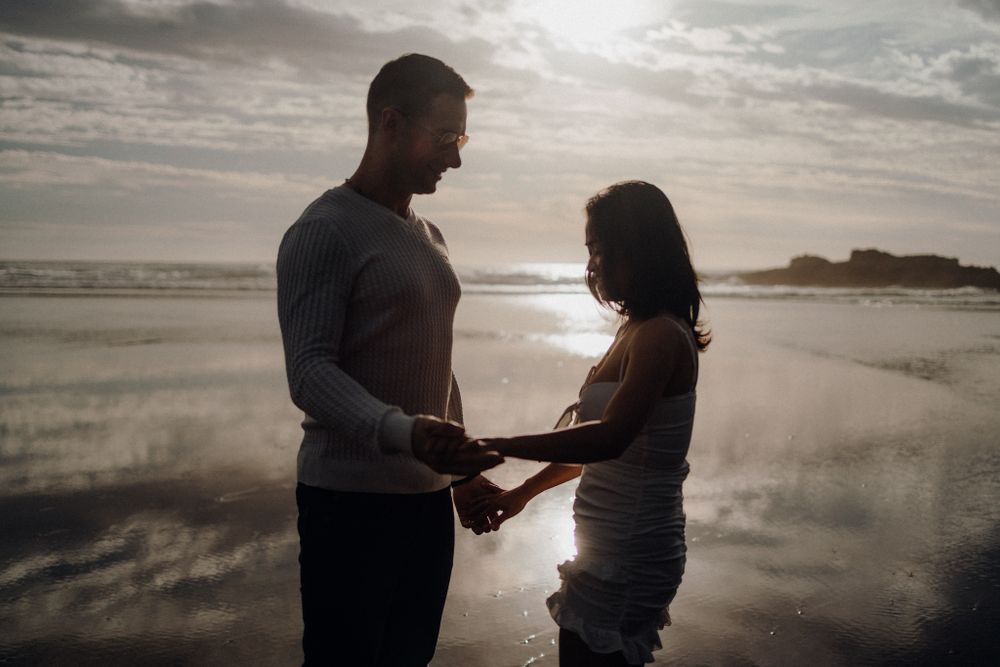 A couple shares a romantic moment on a reflective beach at sunset.