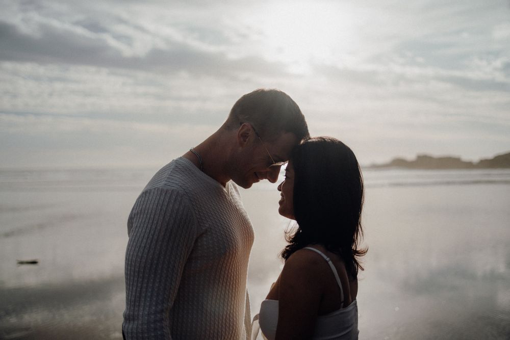 An intimate moment between a couple silhouetted against a misty beach sunset.