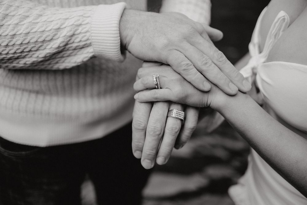 Close-up of hands displaying wedding rings in black and white photography.