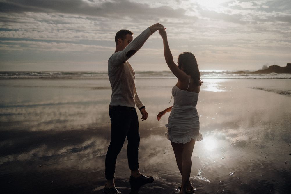 A couple dances together on a misty beach during golden hour.