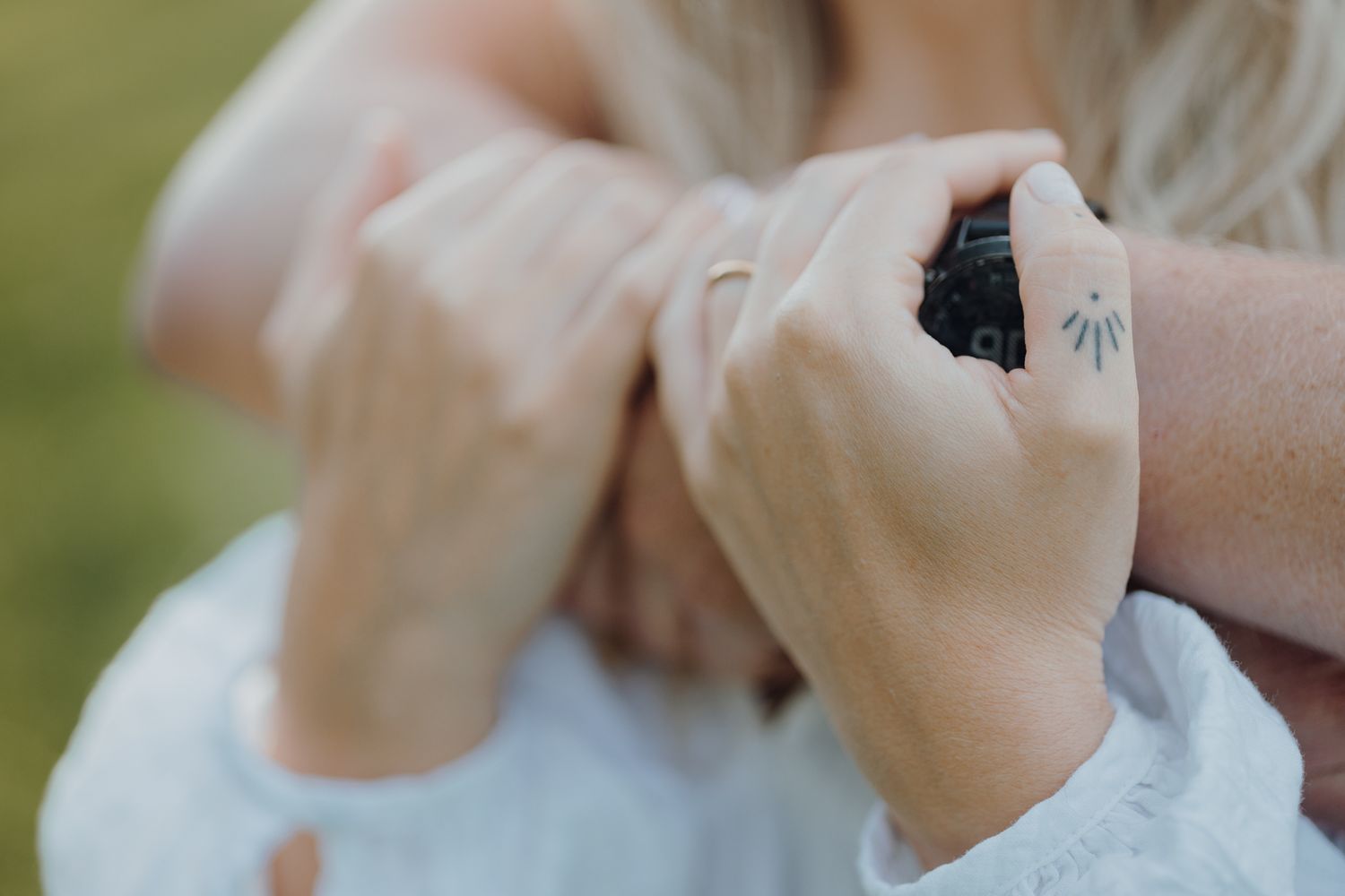 Close up of hands holding a small dark object against a white garment.