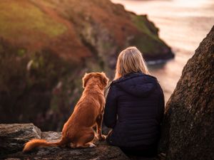 Girl and dog sitting and looking out at the ocean