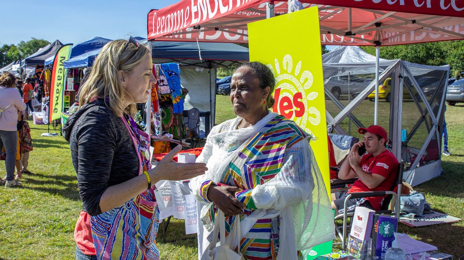 Colorful outdoor market stalls with vendors and tents at a community event.
