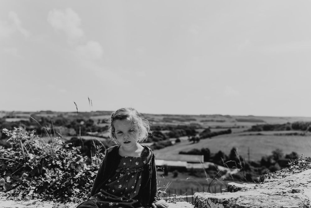 Two year old girl stares into the lens against a countryside landscape.