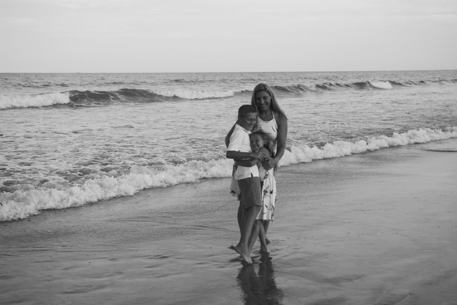 family beach photos smiling and hugging near waves