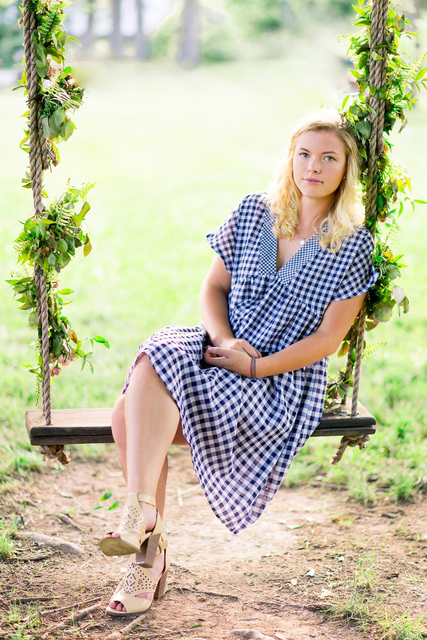 young woman in blue dress leaning against floral rope swing at The Marmalade Lily for senior pictures in Cincinnati