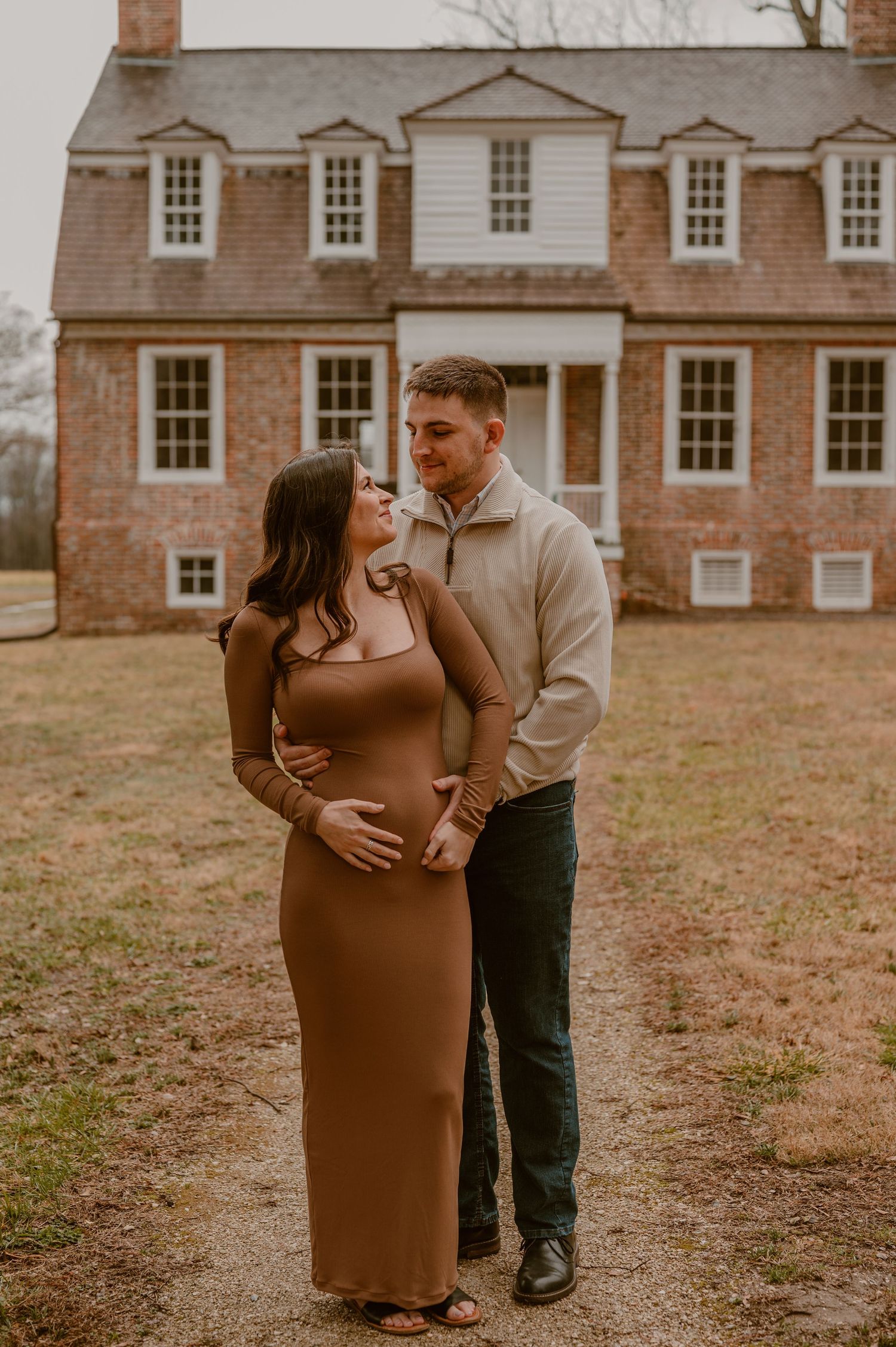 An expecting couple poses in front of a historic brick colonial house during their maternity photoshoot. photo by Samantha Campbell imagery
