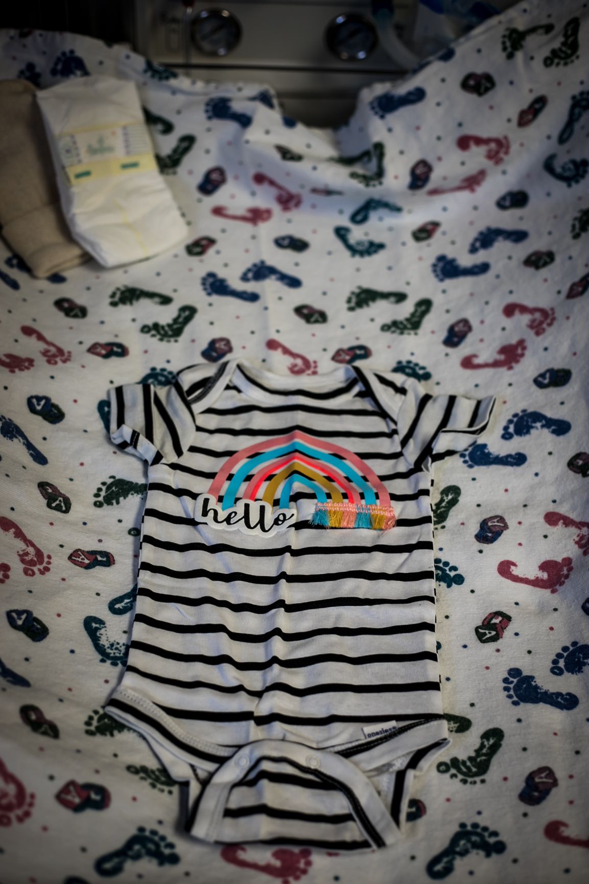 Infant onesie with a rainbow and the word "Hello" on it, laying in the hospital warmer waiting for the baby girl coming.
