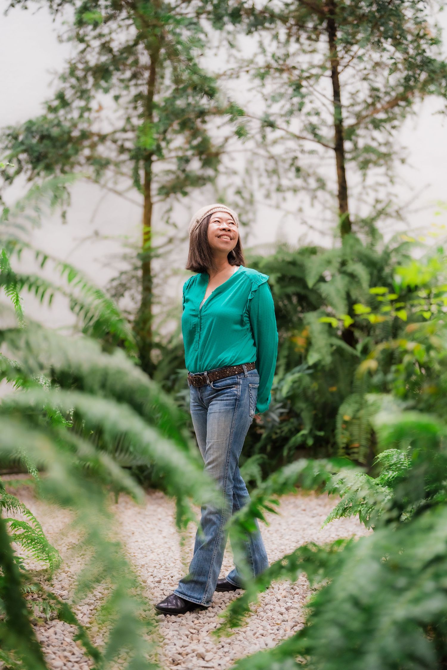 A candid scene in a lush garden path with someone wearing a green top and jeans surrounded by foliage and trees.