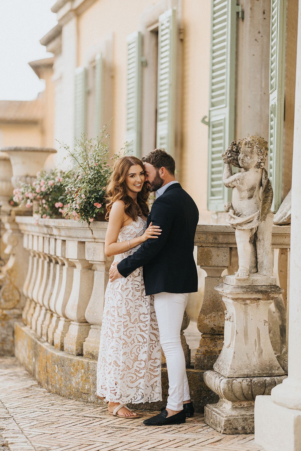 A romantic engagement photo series showing a couple embracing on an ornate balcony with stone railings and decorative urns.