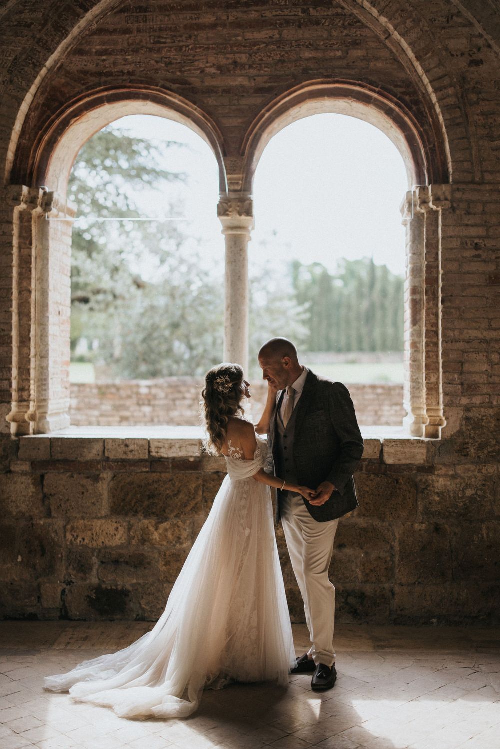 A romantic wedding couple shares intimate moments in a rustic brick archway setting with natural lighting.