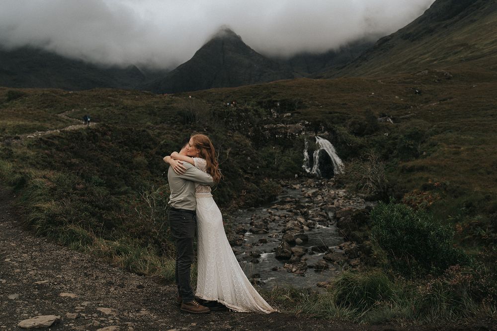 A couple embraces dramatically against a misty mountain landscape in Scotland during their elopement photoshoot.