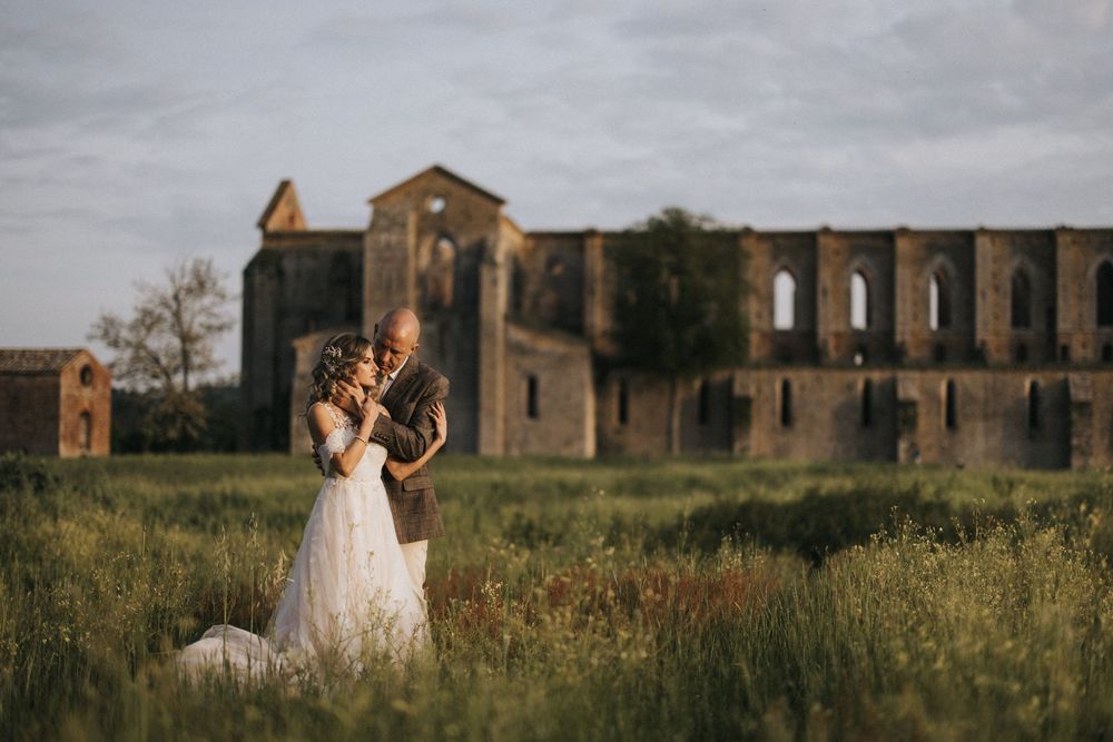 Sun sets behind a romantic photoshoot at historic stone ruins surrounded by green grass and flowers.