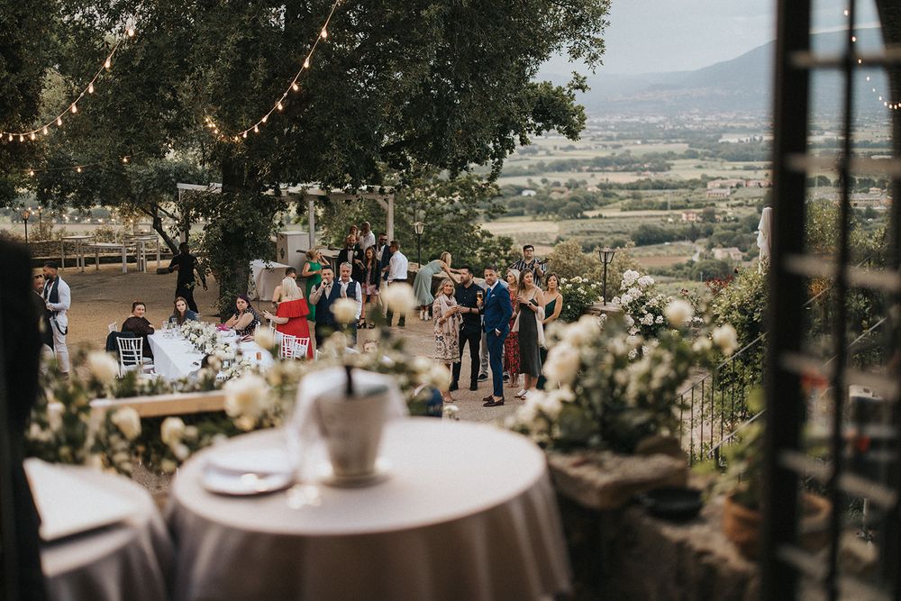 An outdoor wedding reception setup with string lights and round tables overlooking a scenic valley view.