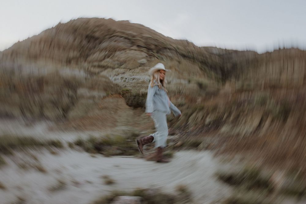 Dreamy artistic portrait of someone in a flowing dress walking through foggy coastal dunes at sunset.