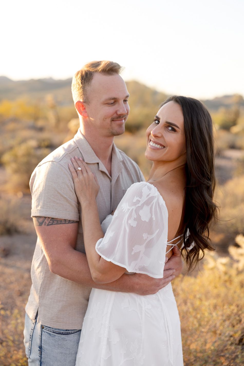 A joyful couple embraces and laughs together in a sun-drenched desert setting at golden hour.
