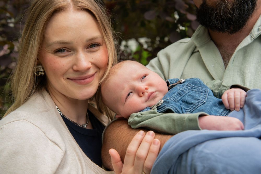 A loving couple shares tender outdoor moments while cradling their newborn baby in natural lighting.