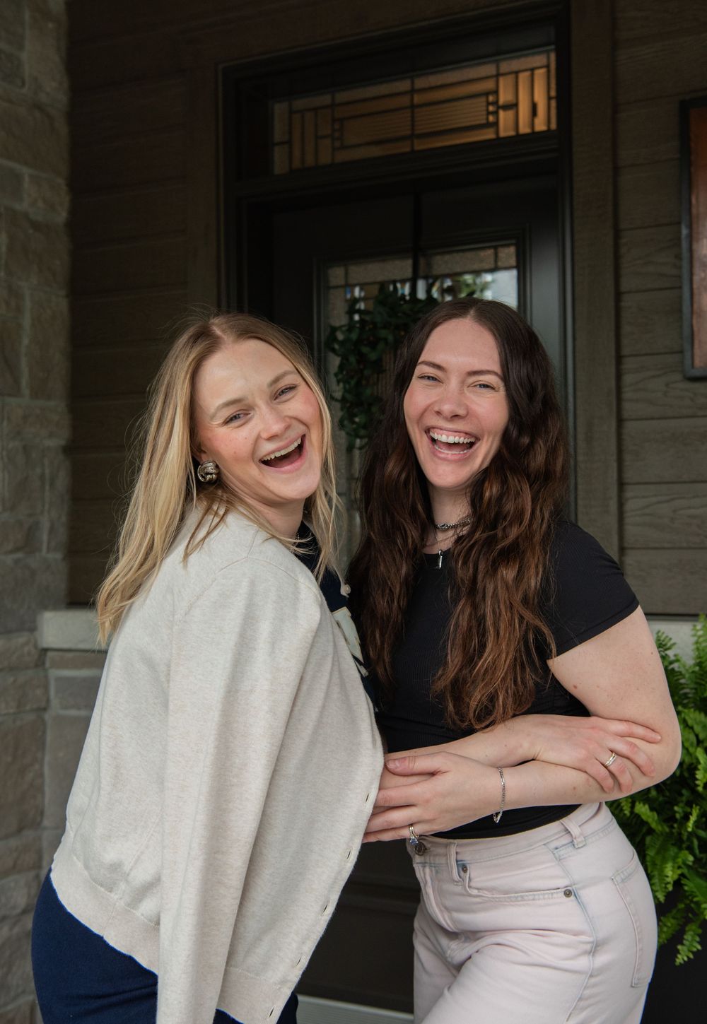 Two friends share a heartfelt laugh together while embracing on a front porch.