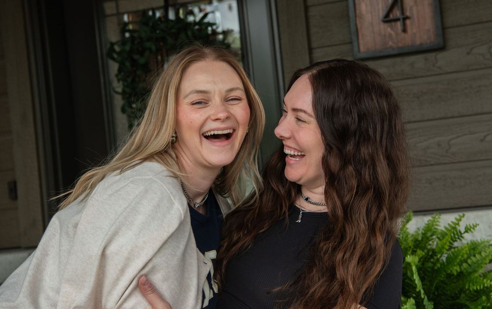 Two friends share a joyful moment of genuine laughter together on a porch near a door marked number 4.