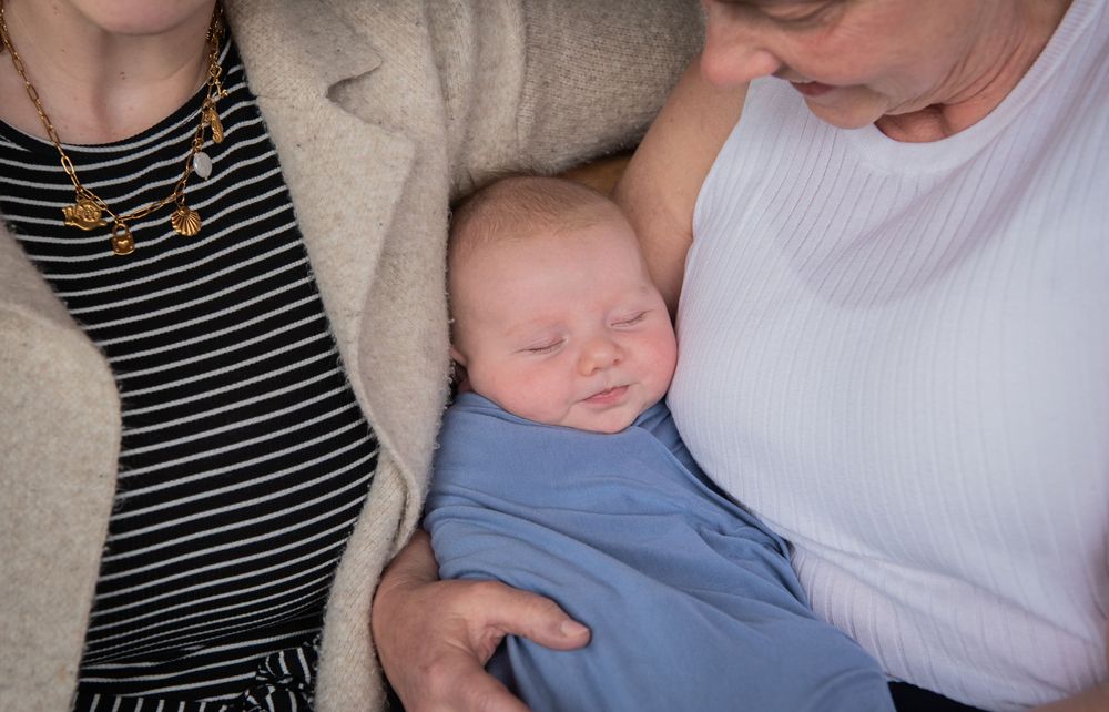 A sleeping baby in blue clothing rests peacefully between two adults wearing casual attire.