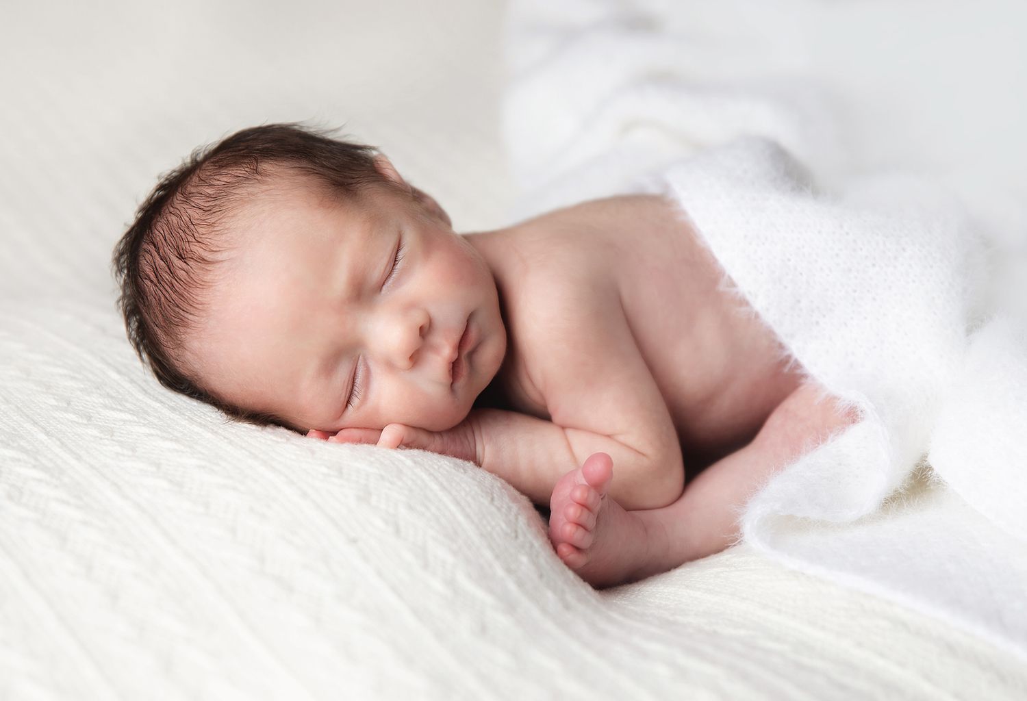 Peacefully sleeping newborn baby rests on soft white blanket, showcasing delicate features and bare skin. During a newborn shoot in Bexley