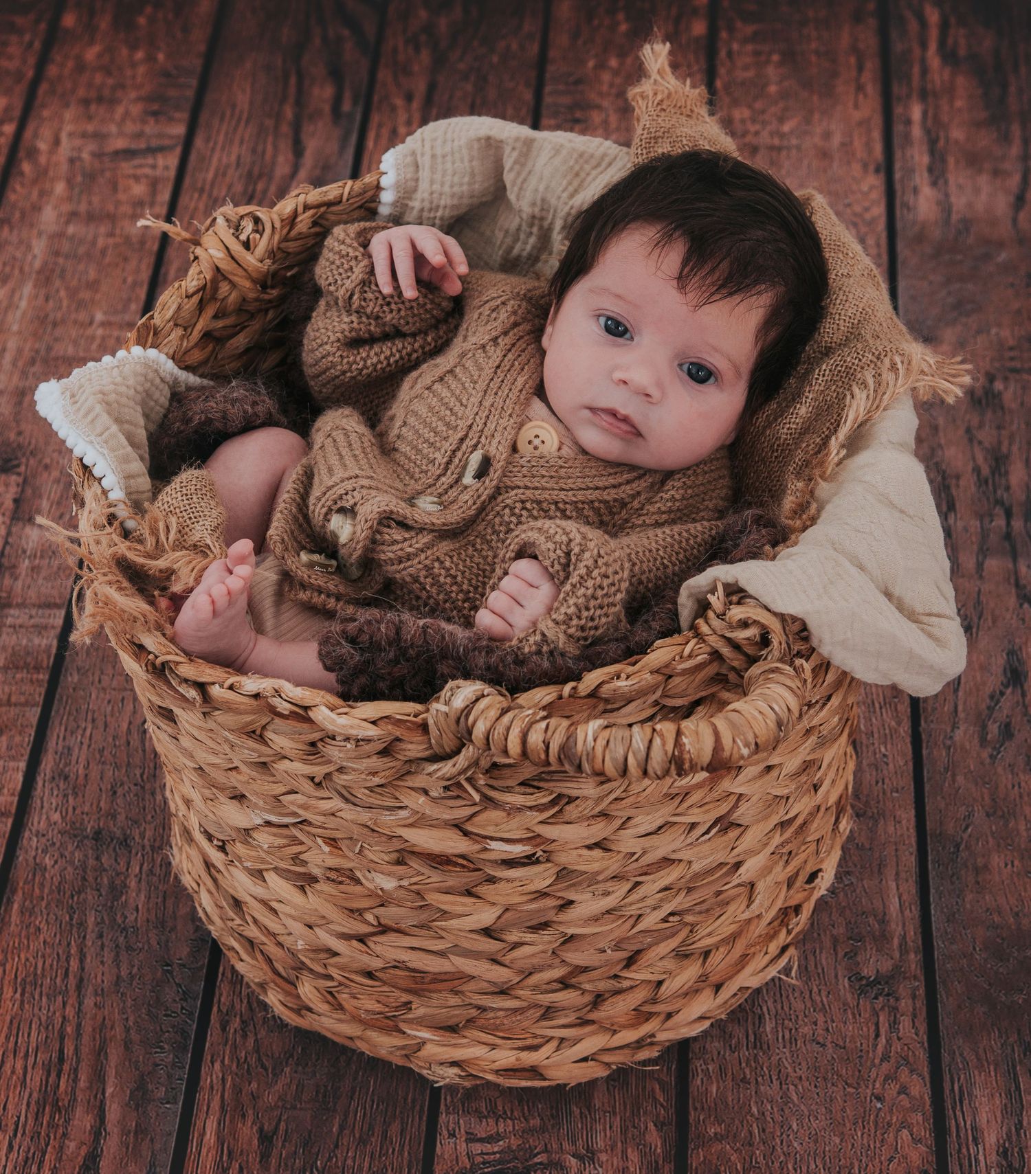 Newborn baby girl in basket with big beautiful eyes looking at camera by Devon newborn photographer Melanie Barnfield