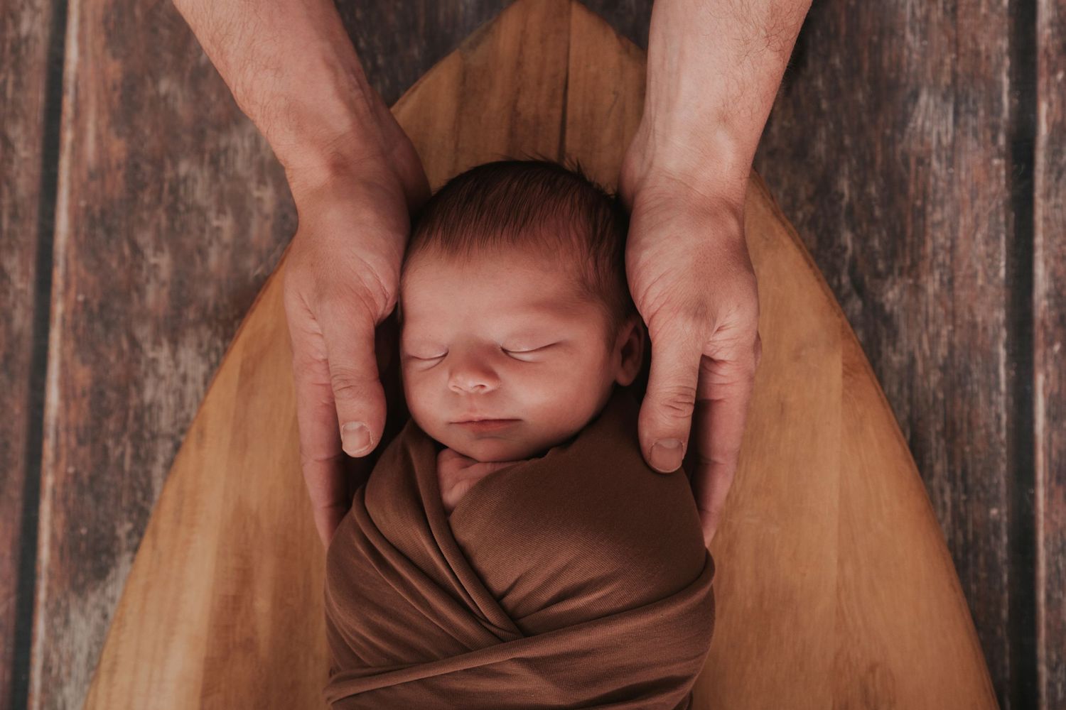 Newborn baby on surfboard with her daddy's hands holding her by devon newborn photographer Melanie Barnfield