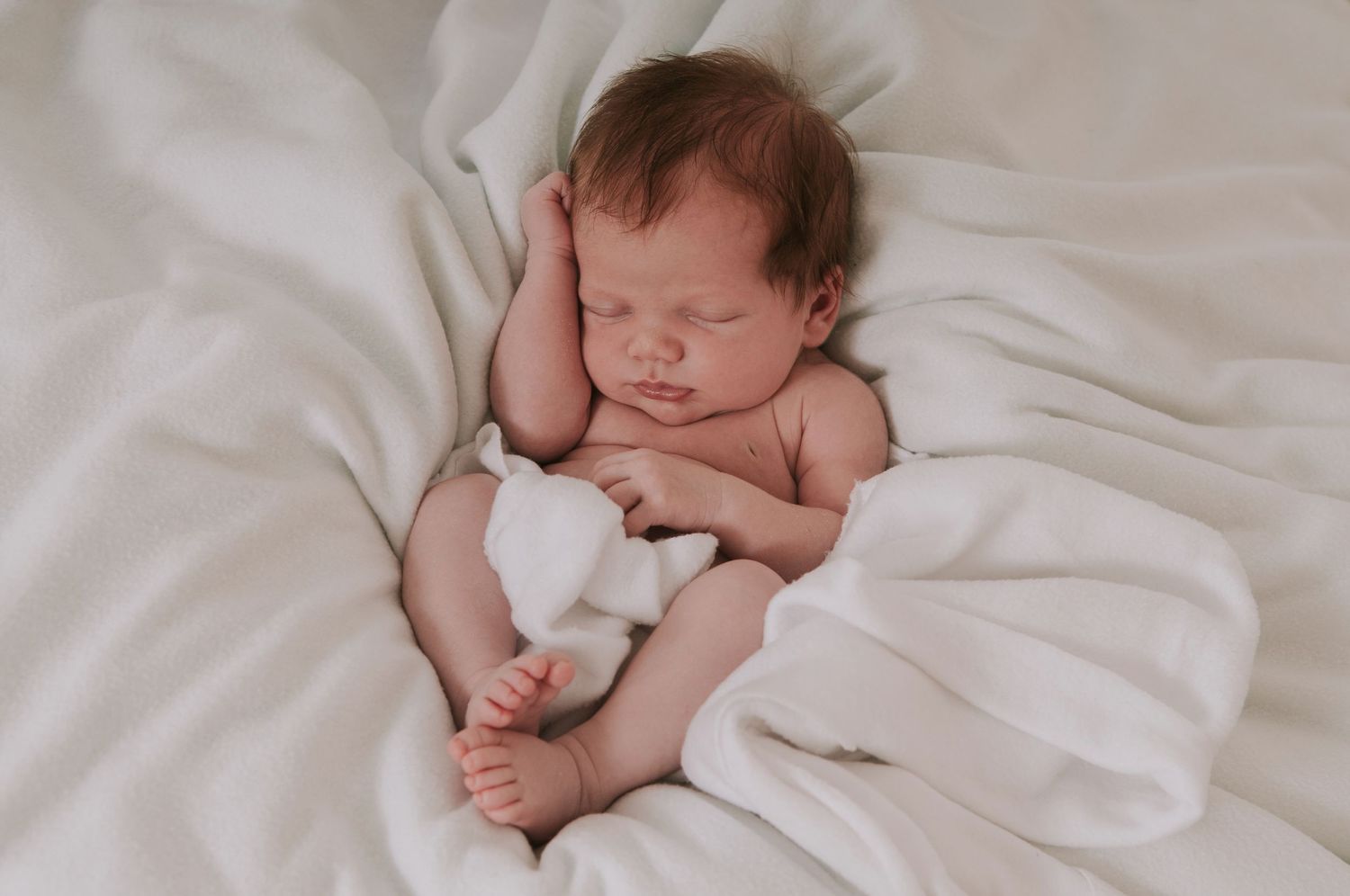 Sleeping newborn snuggled in white by devon based photographer Melanie Barnfield