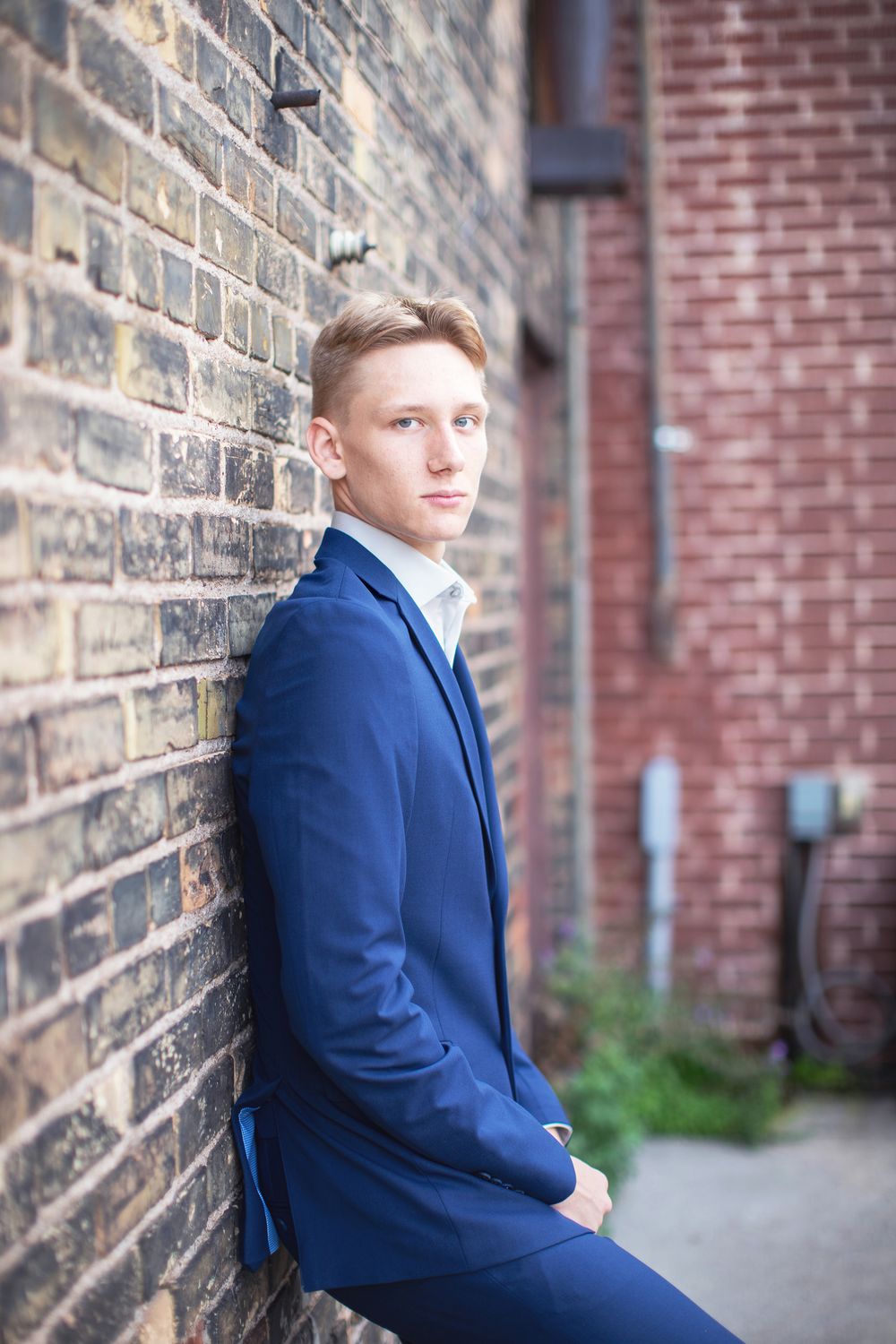 Professional portrait against rustic brick wall featuring someone in a navy blue suit looking contemplative.