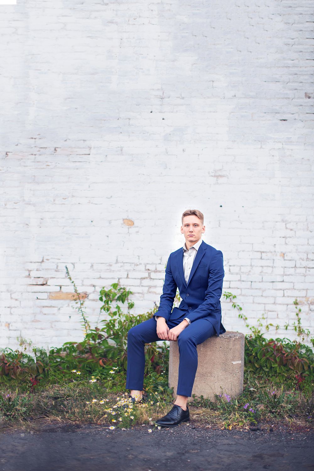 A series of photos showing a person in a blue suit posing against a white painted brick wall with ground vegetation.