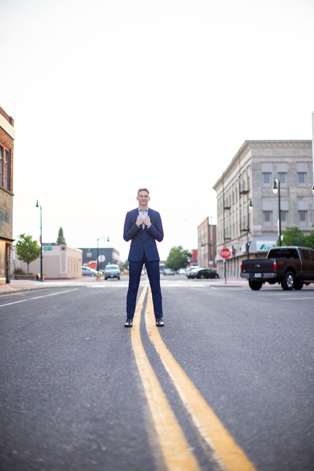 Person in navy blue suit standing on double yellow lines in middle of small town street with buildings in background.