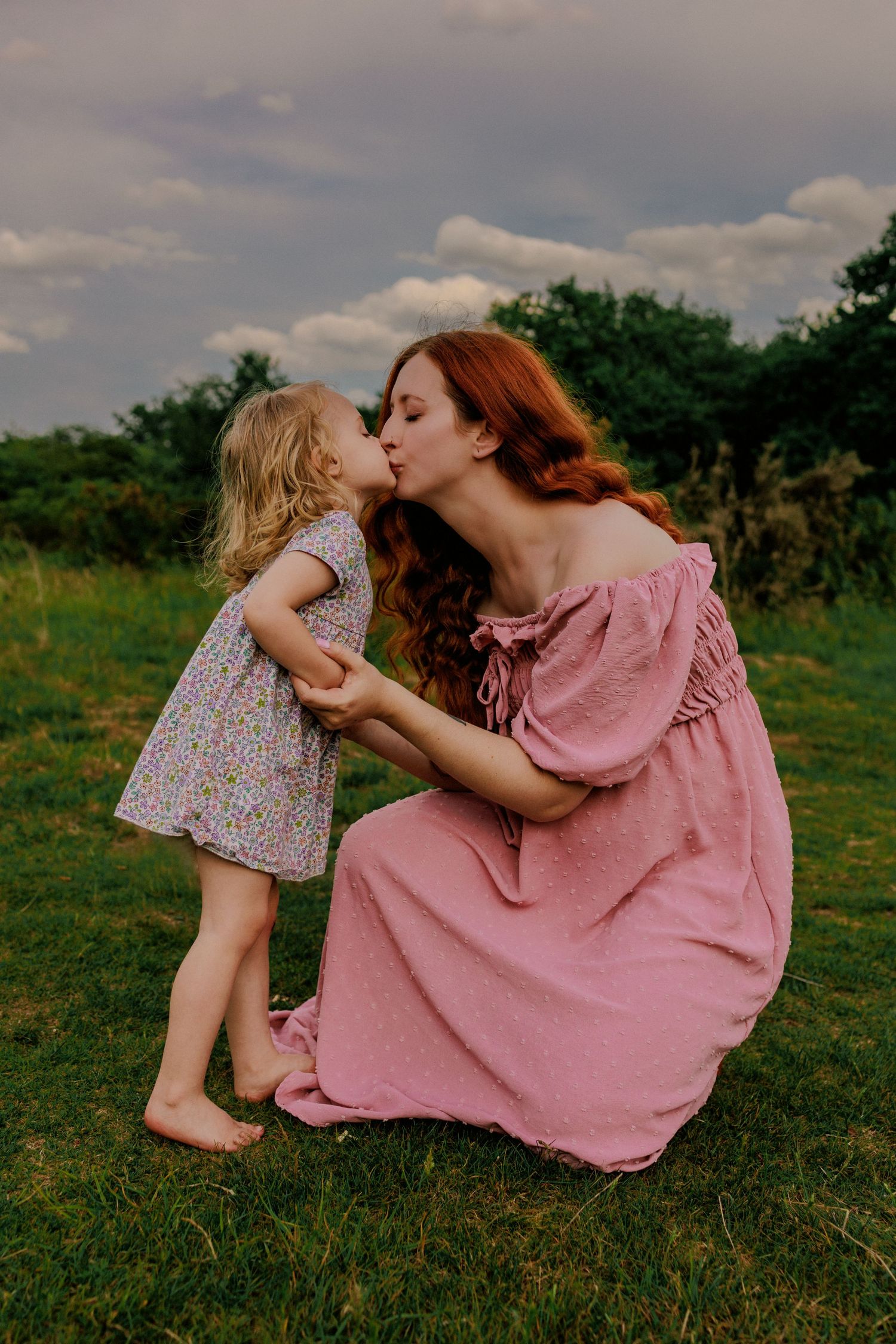 red head pregnant mother and toddler sharing a tender kiss in fields ,vivid colour, norfolk, natural lighting. maternity