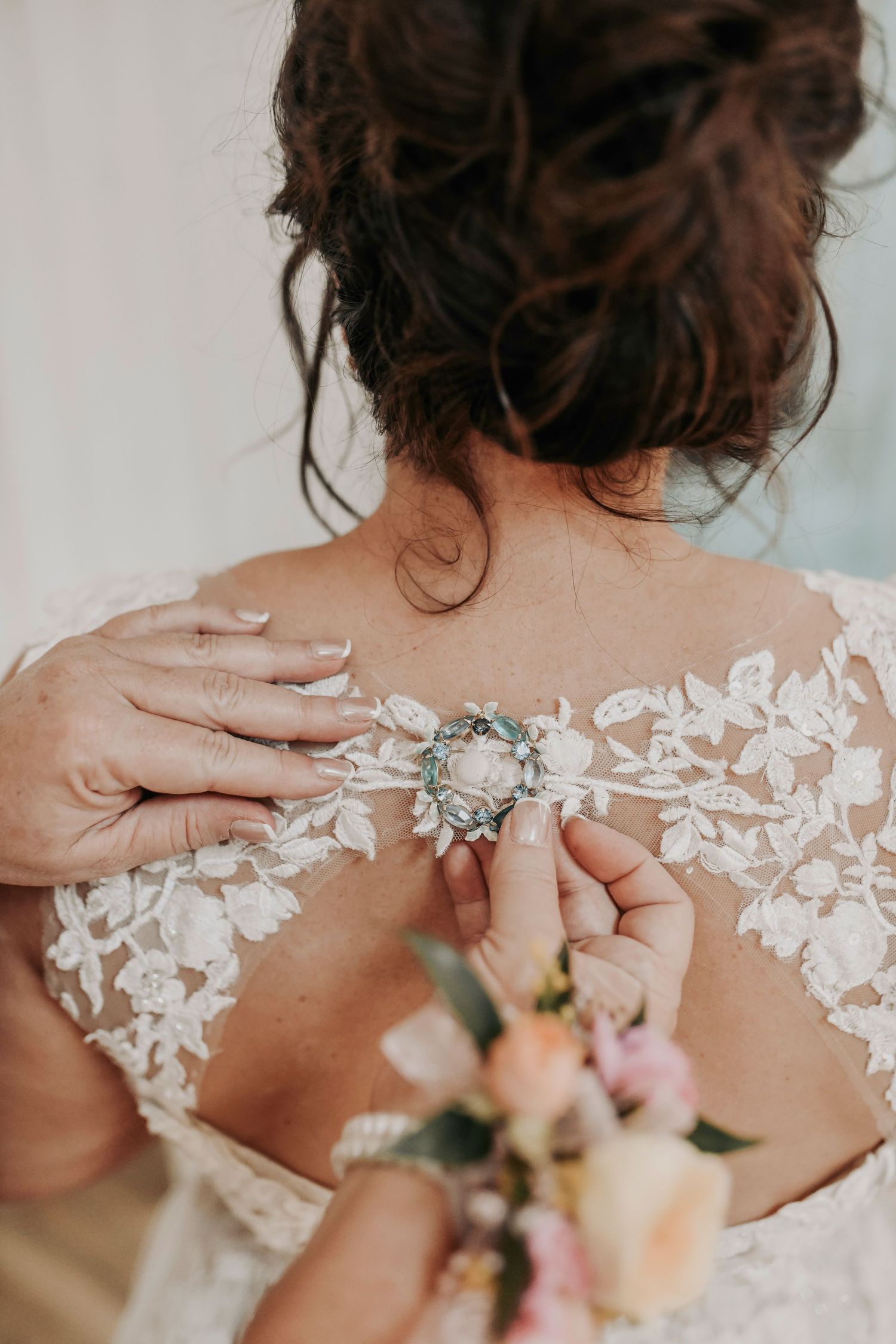 Mother of the bride placing a vintage brooch on the bride’s gown