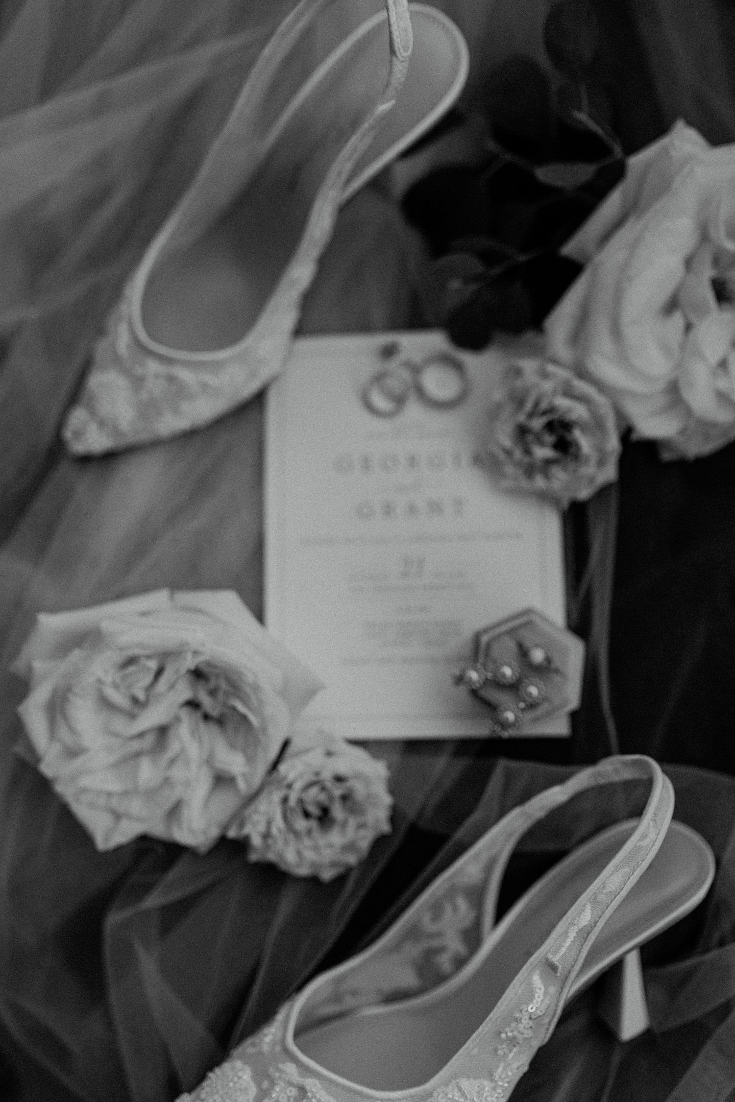 Elegant black and white photograph showcasing scattered wedding flower petals beside formal shoes.