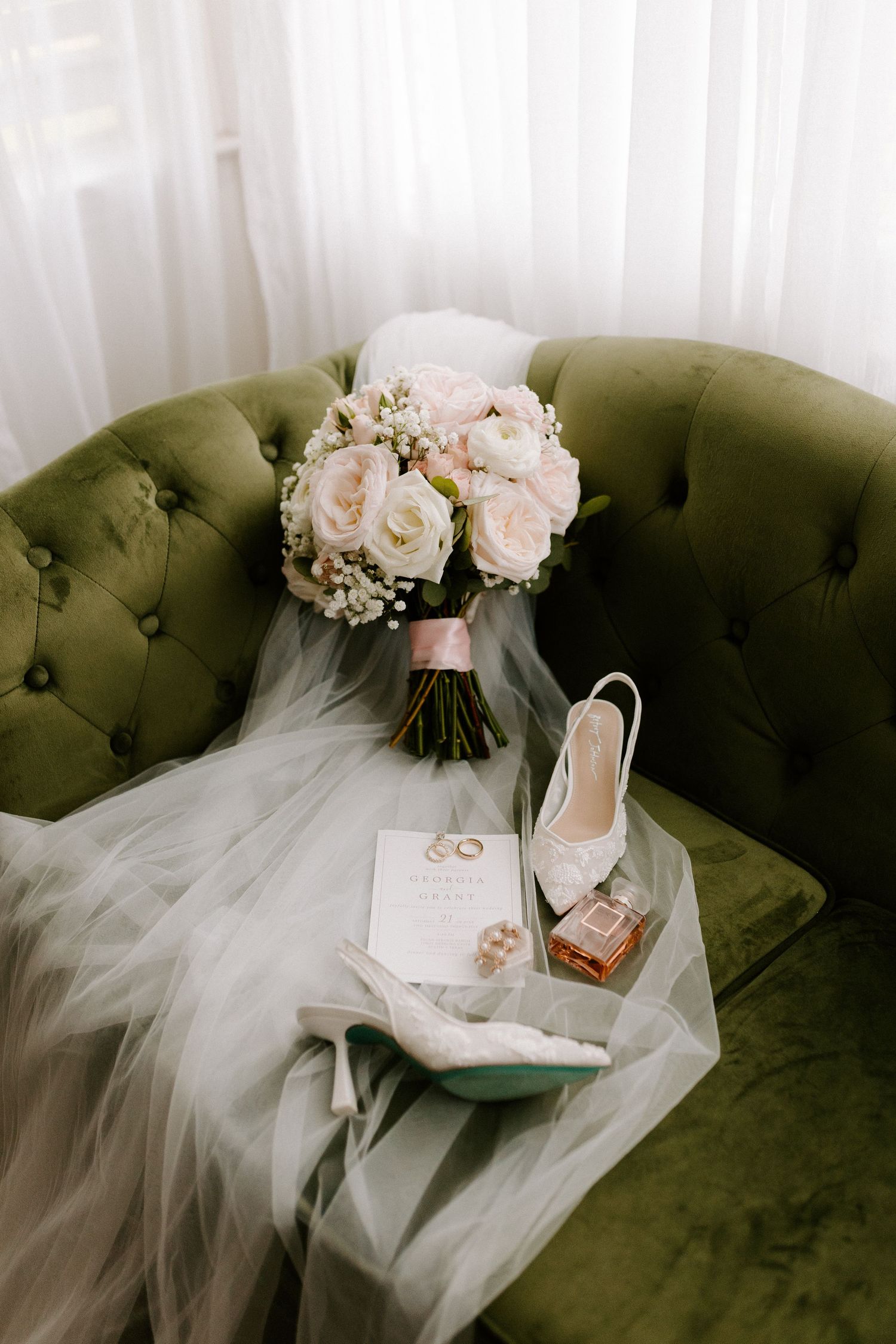 Wedding details with white roses bouquet, shoes and invitation on emerald green velvet couch.