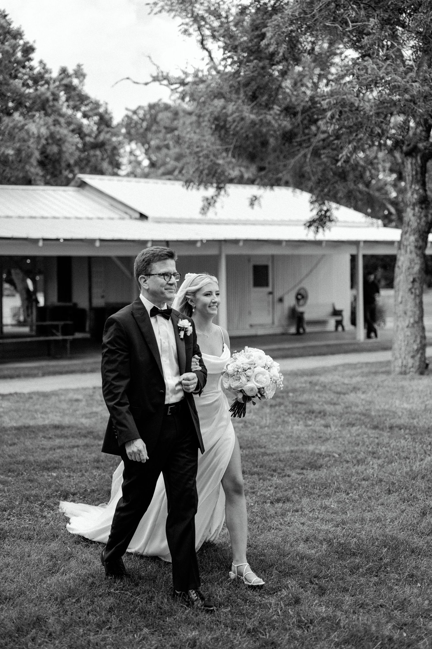 Black and white wedding portrait showing a couple in formal attire outside a rustic venue.