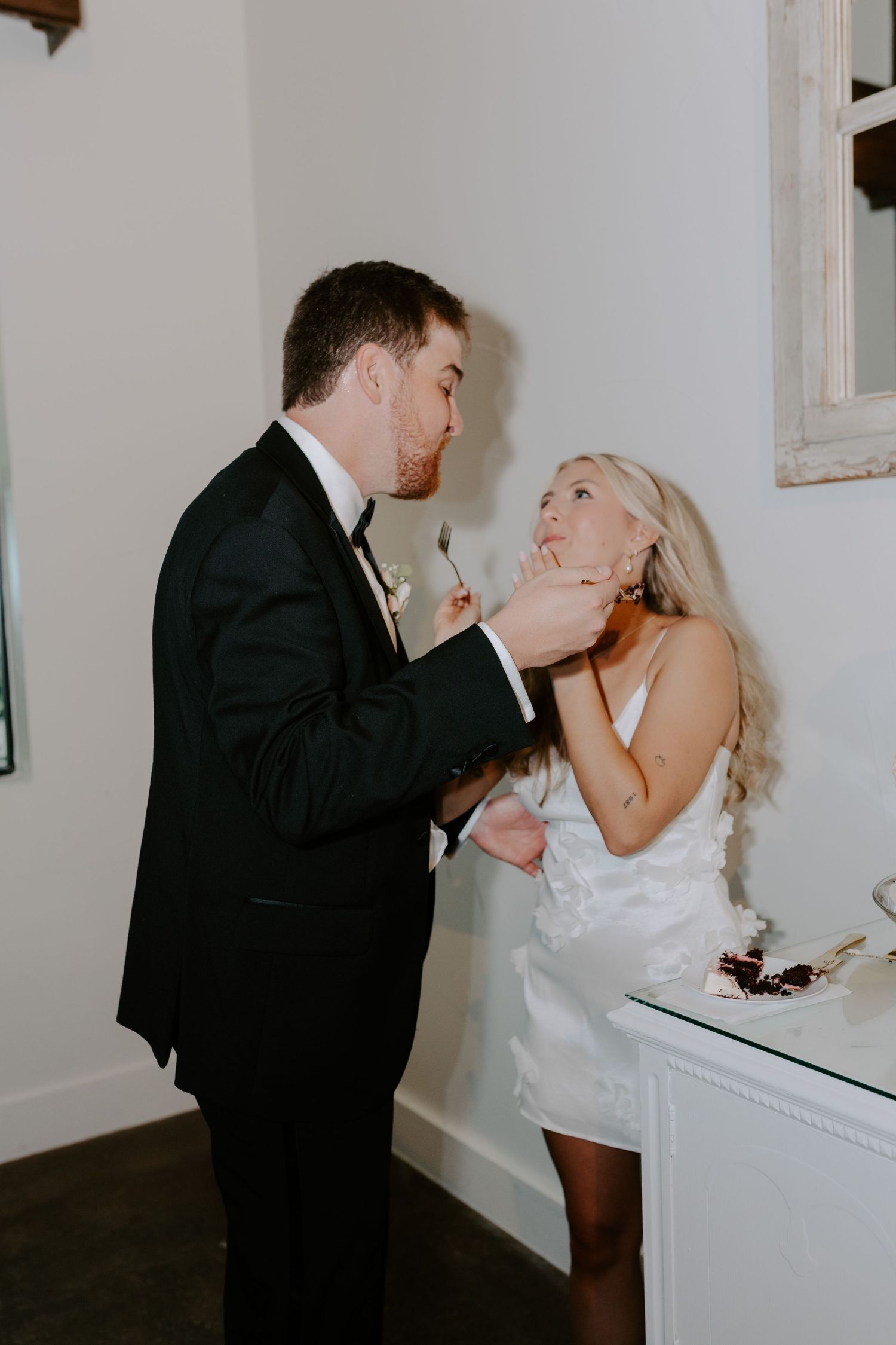 Playful wedding couple shares a fun moment indoors against a white wall.