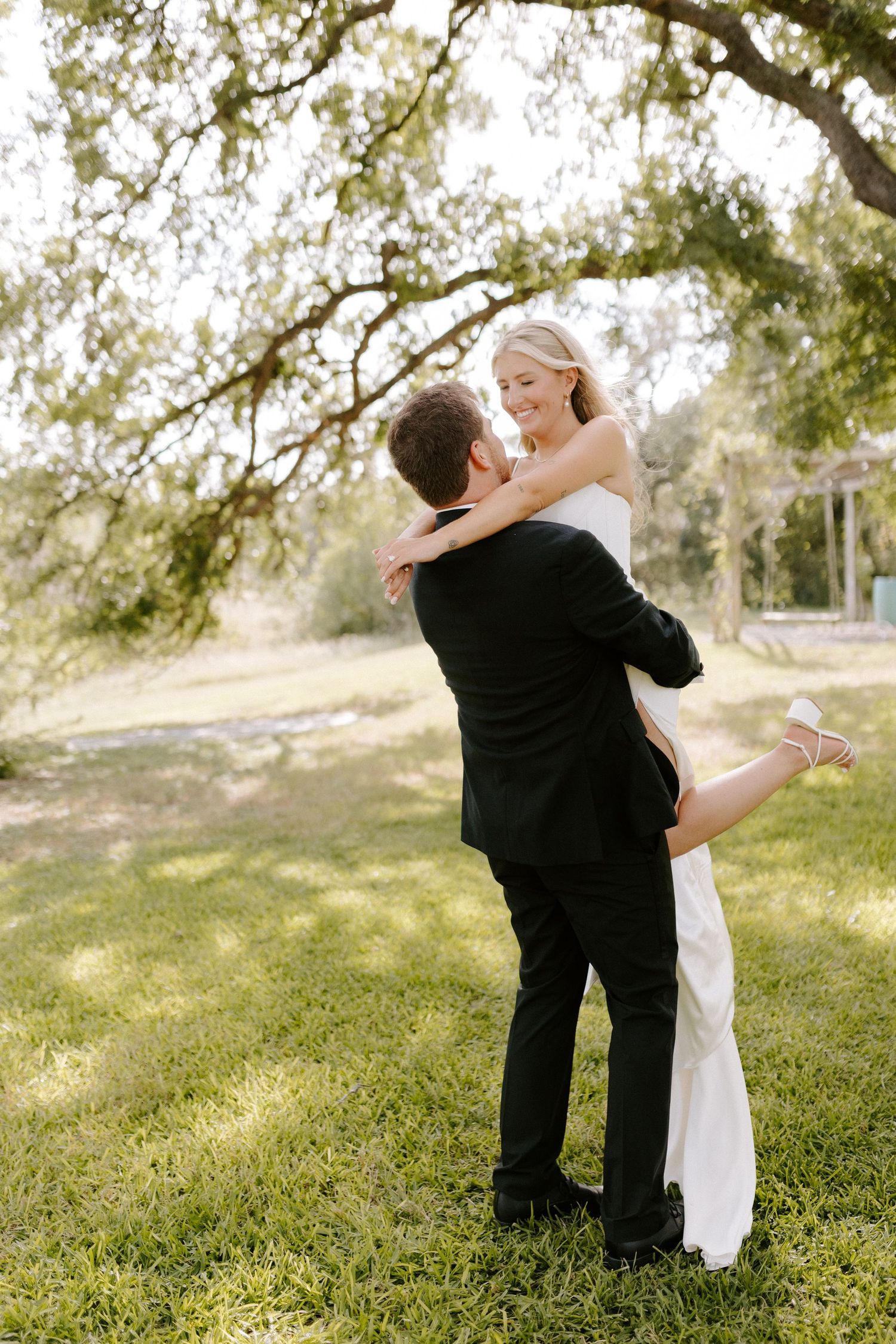 Romantic outdoor wedding scene showing a joyful embrace between newlyweds on a grassy lawn.