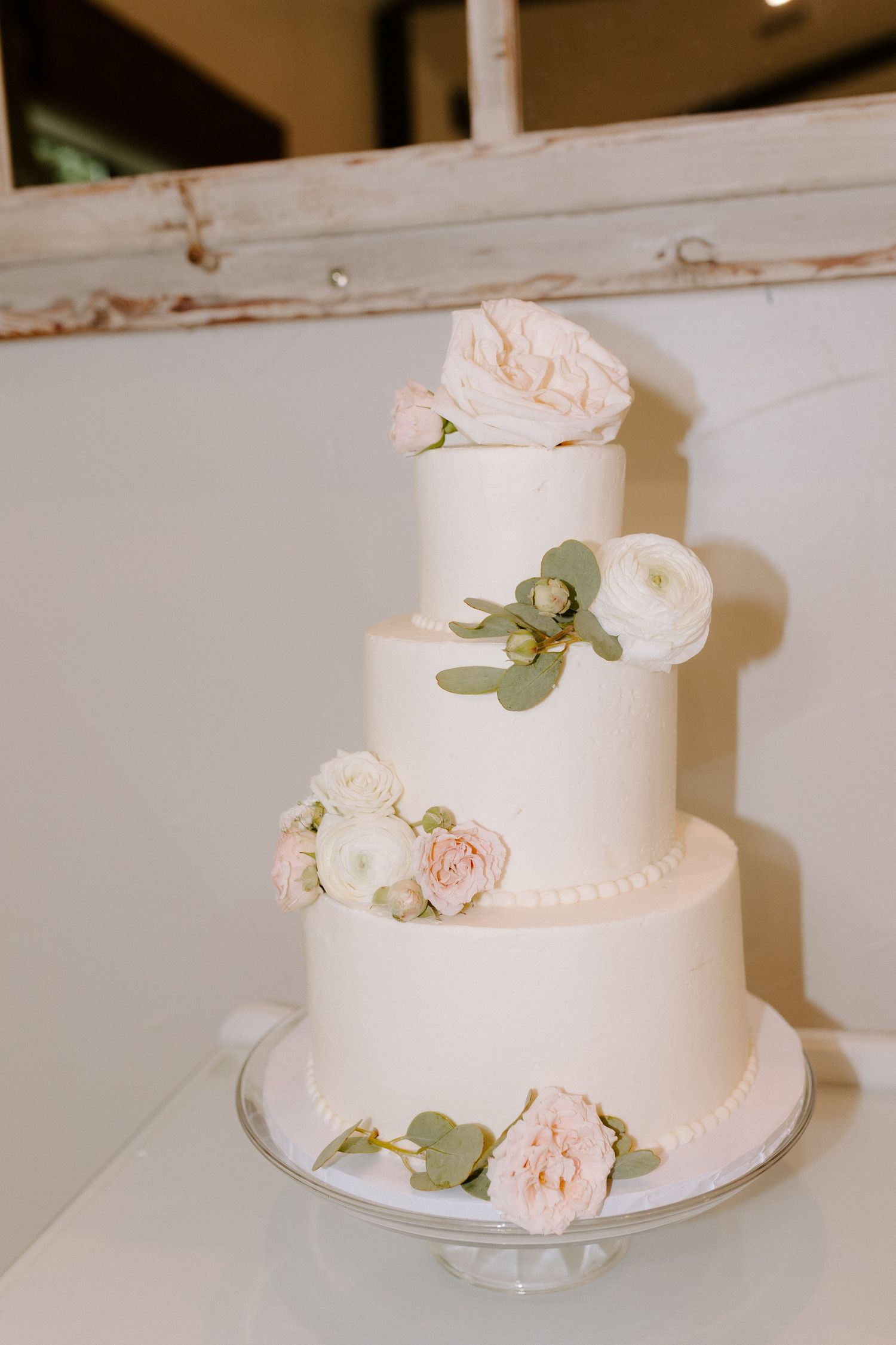 Simple white wedding cake decorated with blush pink roses and eucalyptus leaves.