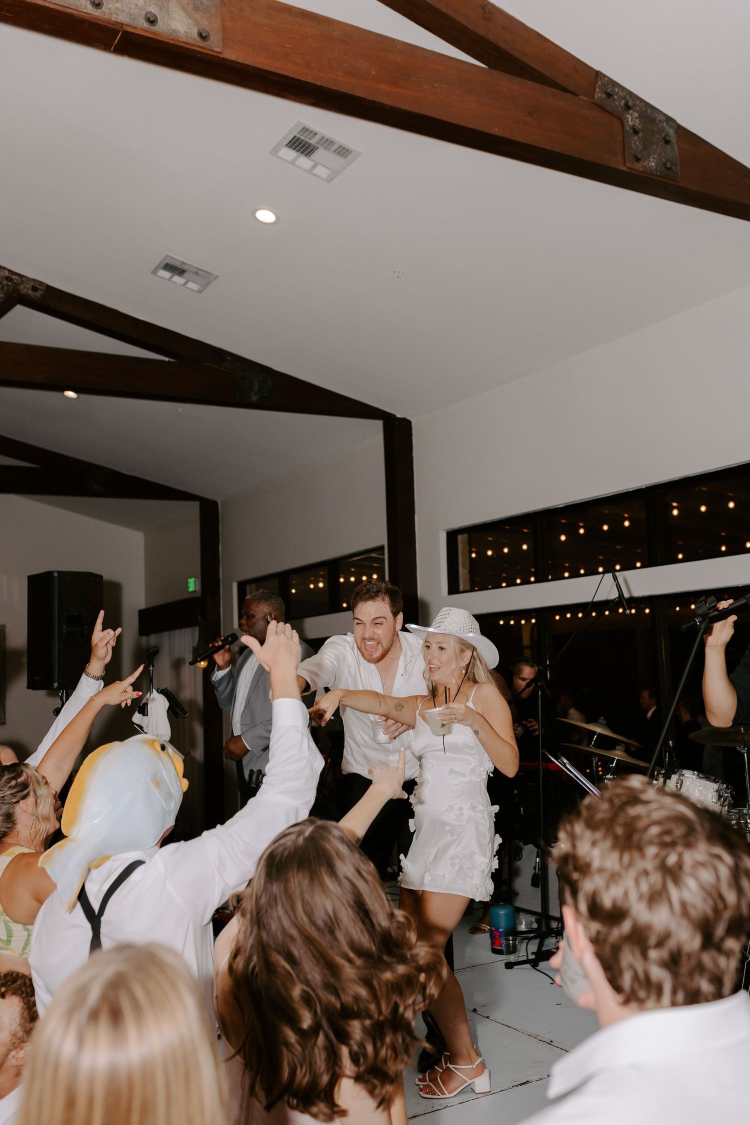 Wedding celebration with guests dancing and cheering on a white-clad couple during a lively reception party.