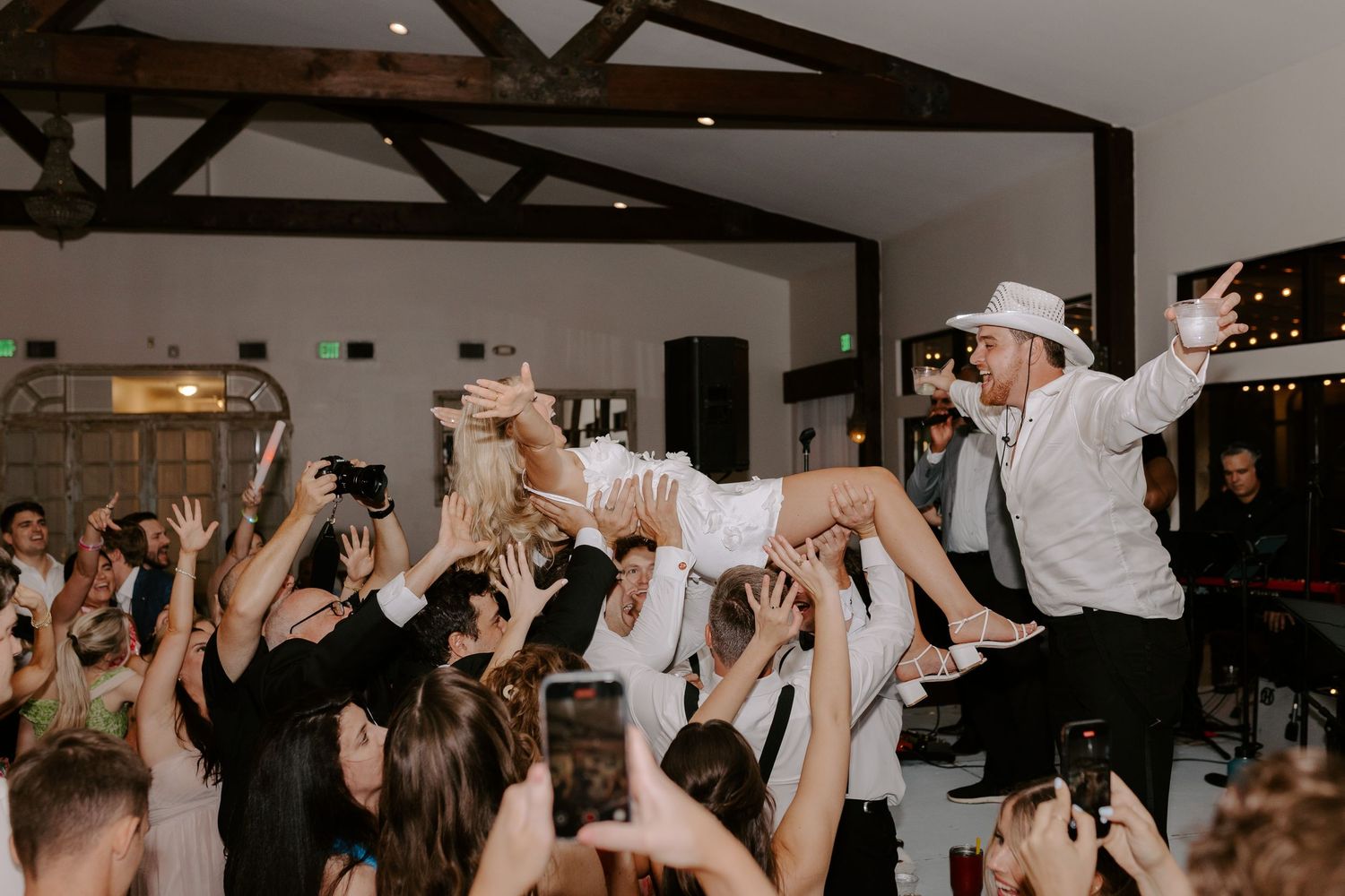 Energetic wedding reception scene with crowd surfing and dancing guests.